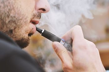 Homem barbado soltando fumaça ao usar um cigarro eletrônico