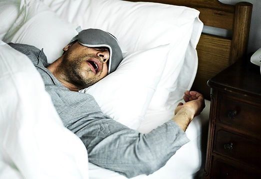 Homem dormindo de boca aberta usando máscara de dormir
