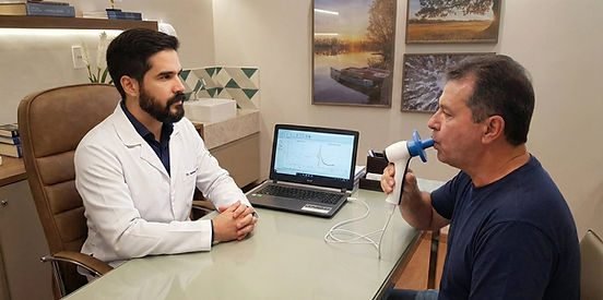 Médico de jaleco acompanha paciente soprando em espirômetro ligado a um notebook