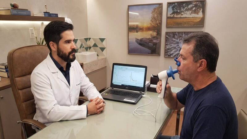 Pessoa realizando espirometria com clipe nasal e bocal, orientada por profissional de saúde.